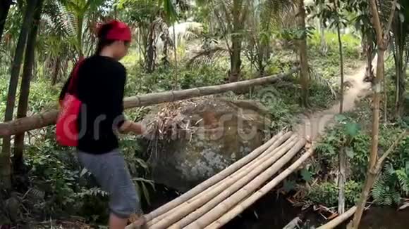 年轻漂亮的女士穿过竹桥穿过充满自然植被的春河视频的预览图