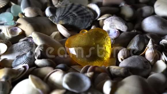 黄色的玻璃心躺在大海的卵石上特写高细节轮换4K视频的预览图