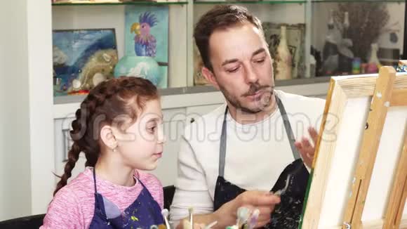 可爱的小女孩看着她父亲的艺术家画一幅画视频的预览图