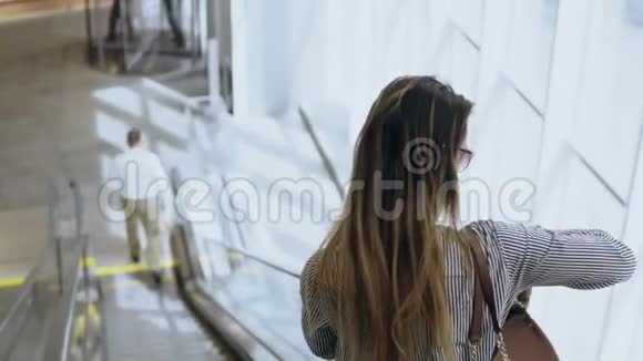 年轻美丽的女人站在自动扶梯下使用智能手机准备见面视频的预览图