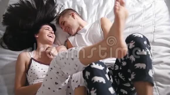 快乐的恋人在床上微笑着互相抚摸双腿抬起从上面眺望视频的预览图