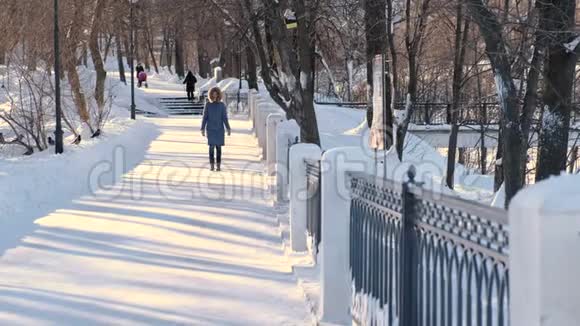 穿着蓝色羽绒服的年轻女子带着毛皮罩在冬季公园散步前景视频的预览图