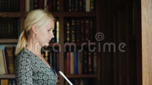一个年轻的女人在图书馆或办公室打扫卫生看起来像书架上的书上的灰尘视频的预览图