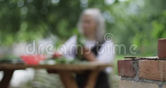 一位头发灰白的老妇人坐在花园的一张桌子旁手里拿着一个西红柿和一根黄瓜视频的预览图