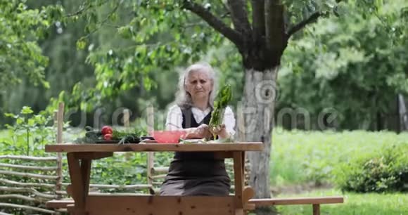 一位白发苍苍的老妇人正坐在花园里的一张桌子旁手里拿着绿叶沙拉视频的预览图