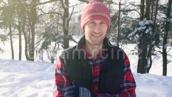 冬天森林里一个穿着红色衬衫和帽子微笑的男人的肖像视频的预览图