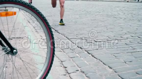 运动员们沿着铺好的路奔跑经过一个骑自行车的人从自行车的轮子上可以看到奔跑的人们城市视频的预览图