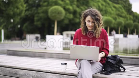 穿红色衣服的年轻女子在喷泉旁用笔记本电脑工作视频的预览图