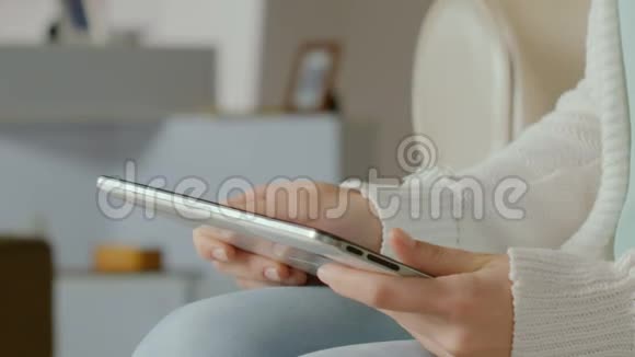 女性坐在沙发上在平板电脑上浏览新的应用程序特写视频的预览图