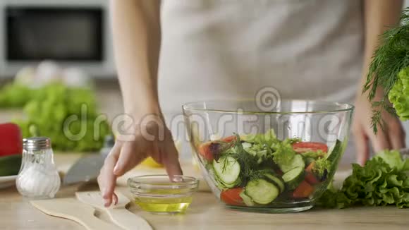 在新鲜制作的蔬菜沙拉中加入橄榄油使女性的双手紧紧抓住视频的预览图