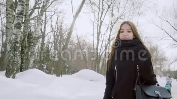 一个年轻女人的冬天画像一个没有头饰的女孩走过冬天的公园视频的预览图