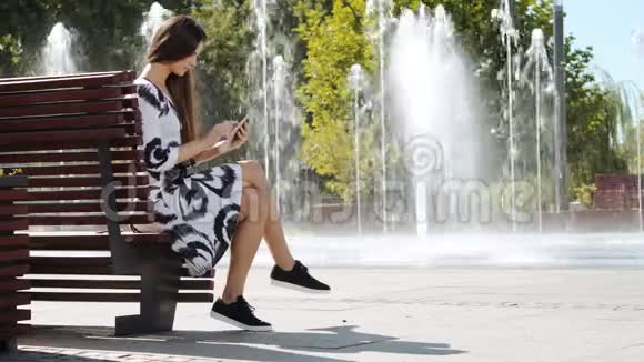 年轻的女商人穿着连衣裙坐在长凳上在平板电脑上工作视频的预览图