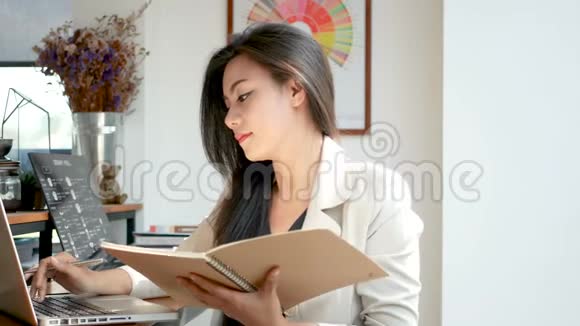 4K镜头美丽的亚洲商务女性坐在电脑手提电脑键控数据阅读和翻页笔记簿页面视频的预览图
