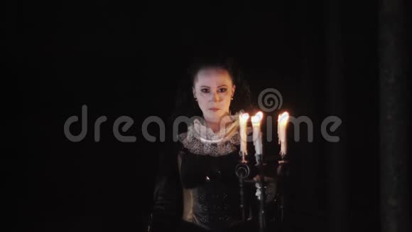 神秘的女人穿着维多利亚式的裙子用烛台盯着黑暗的房间视频的预览图