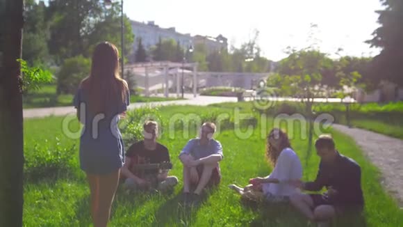 在夏天公园里一位年轻的女士在坐在草地上的朋友面前表演哑剧视频的预览图