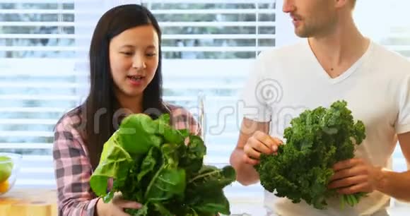 一对怀孕的夫妇在厨房里拿着新鲜的绿叶蔬菜视频的预览图