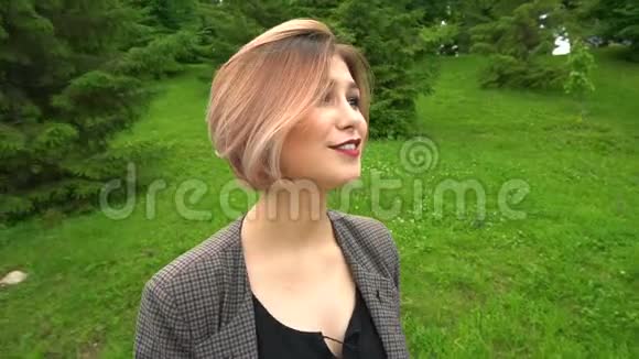 慢动作快乐微笑的年轻女子穿着夹克在阳光明媚的公园散步夏天视频的预览图