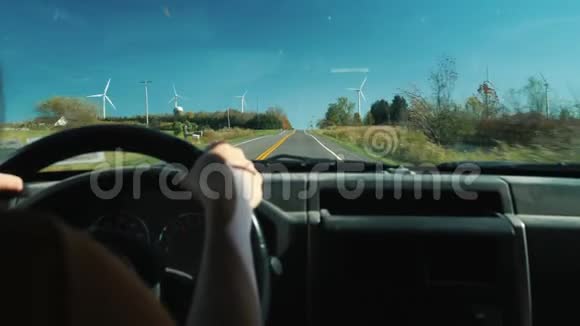 驾驶汽车的司机在农村公路上行驶侧面有许多风力涡轮机生态旅游和清洁视频的预览图