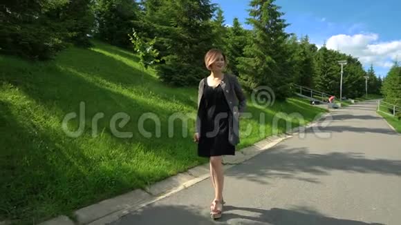 慢动作快乐微笑的年轻女子穿着黑色连衣裙在阳光明媚的公园散步夏天慢节奏视频的预览图