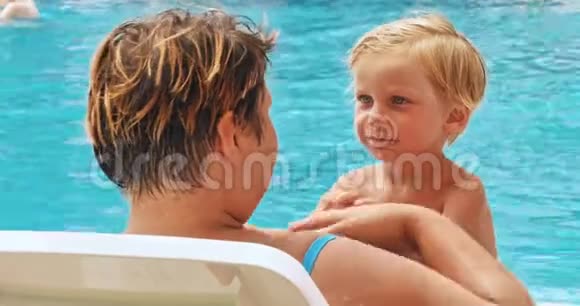 母亲和儿子在度假村游泳池附近的日光浴中放松视频的预览图