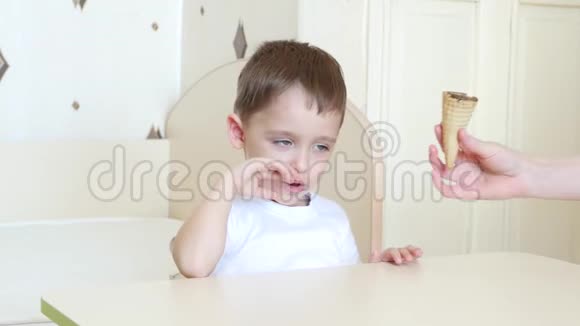 孩子坐在桌旁愉快地在华夫饼锥里吃着巧克力冰淇淋这孩子很快乐视频的预览图