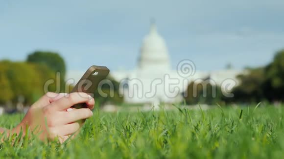 有智能手机的女性手在草坪上在华盛顿国会大厦的背景下旅行和学习视频的预览图