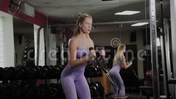 有着美丽身材的运动女人女孩在健身房的模拟器上训练二头肌视频的预览图