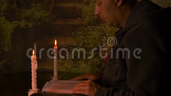 成年白种人读一本书一支燃烧的蜡烛在桌子上配对蜡烛温暖的夜晚在室内视频的预览图