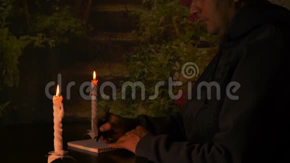 成年白种人用钢笔在笔记本上画画烛光照亮了他的脸商人在书上画平分计划视频的预览图