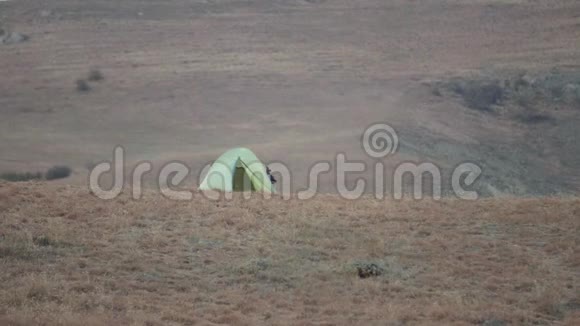 一顶绿色的帐篷矗立在一座红色的小山上山风吹在山顶上视频的预览图
