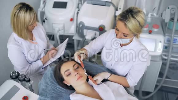 美容师在一家美容院为一位美丽的年轻女性做面部皮肤微电流治疗视频的预览图