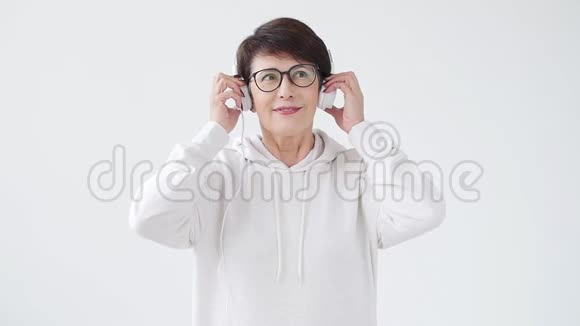热爱音乐的理念成熟的女人用白色背景的耳机播放音乐视频的预览图