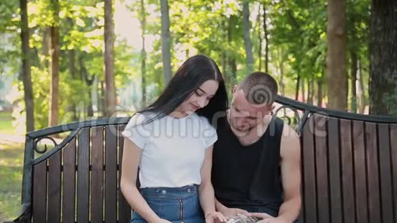 两个情人坐在长凳上互相微笑着看家庭照片视频的预览图