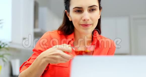 女士在喝柠檬茶的同时使用笔记本电脑视频的预览图