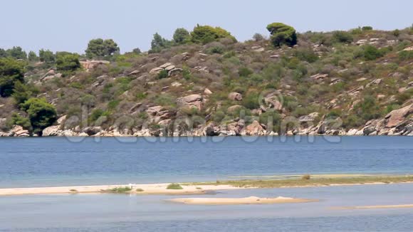 一个田园诗般的海滩和一艘快艇穿过它海边的岩石和树木希腊哈尔基迪基视频的预览图