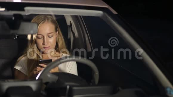 微笑的女人晚上在车里用智能手机视频的预览图
