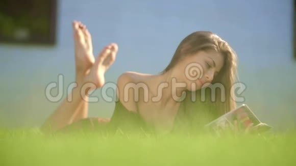 年轻女子躺在草地上读一本慢动作的书关门视频的预览图