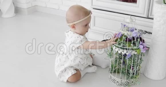 一个可爱的婴儿坐在白色的地板上玩一个装饰笼子视频的预览图