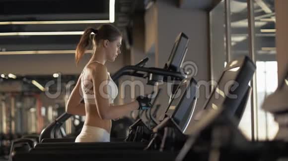 运动妇女使用跑步机屏幕设置健身俱乐部有氧运动视频的预览图