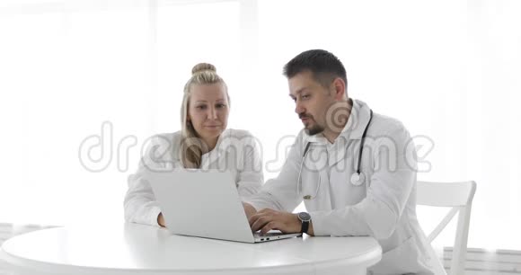 一名身穿白大褂的男性和女性医生使用无线笔记本电脑诊断治疗视频的预览图