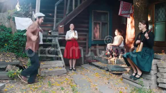 一个男人跳着俄罗斯民族舞蹈女人坐在乡间别墅附近的楼梯上看着他视频的预览图