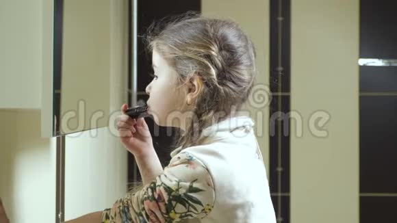 可爱的小女孩在浴室的镜子前用口红涂嘴唇视频的预览图