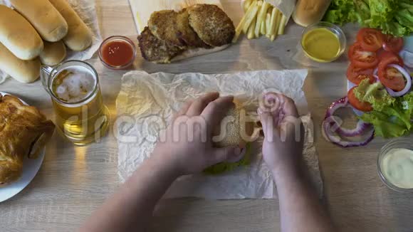 肥胖男人在他的汉堡里添加脂肪炸排不健康的饮食俯视图视频的预览图