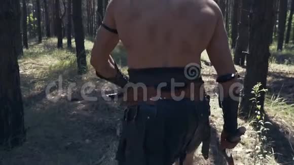 有两把斧头的肌肉战士正在阳光明媚的一天在森林里散步视频的预览图