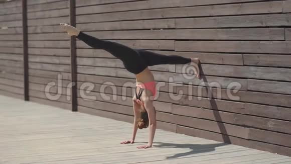 在阳光明媚的日子里女人在墙上练习瑜伽倒立姿势视频的预览图
