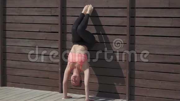 在阳光明媚的日子里女人在墙上练习瑜伽倒立姿势视频的预览图