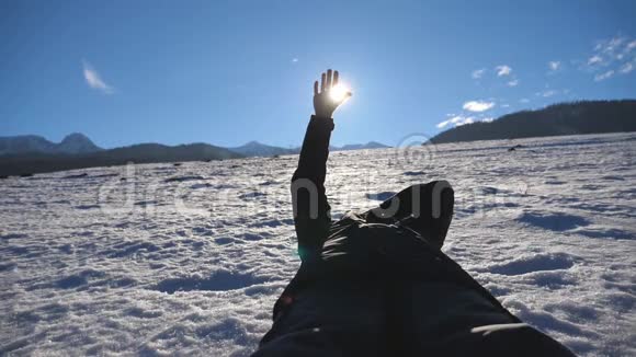 一个面目全非的人躺在雪地上在阳光明媚的日子里用手指望着灿烂的太阳年轻的手视频的预览图