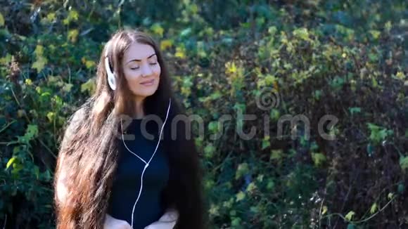 戴着耳机的女人微笑着在户外闭上眼睛欣赏一首歌视频的预览图