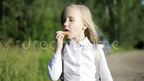 一个饥饿的金发小女孩在沙地路上上学穿过田野吃了一块饼干视频的预览图