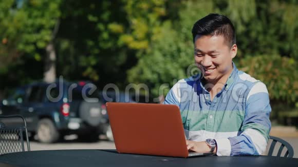 满意的亚洲男人在夏季露台上用笔记本电脑工作视频的预览图